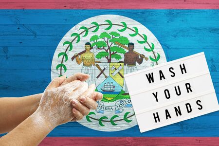 Belize flag background on wooden surface. Minimal wash your hands board with minimal international hygiene concept hand detail.の写真素材