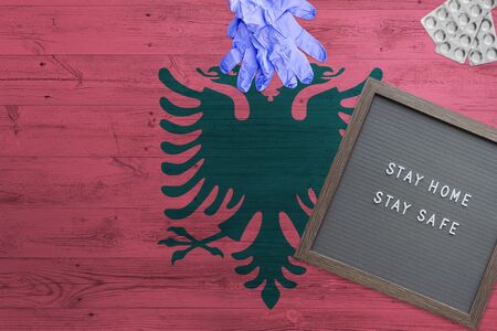 Albania flag background on wooden table. Stay Home writing board, surgery gloves, pills with minimal...