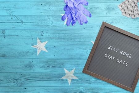 Micronesia flag background on wooden table. Stay Home writing board, surgery gloves, pills with...