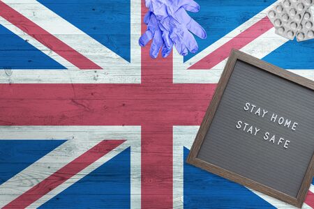 United Kingdom flag background on wooden table. Stay Home writing board, surgery gloves, pills with...