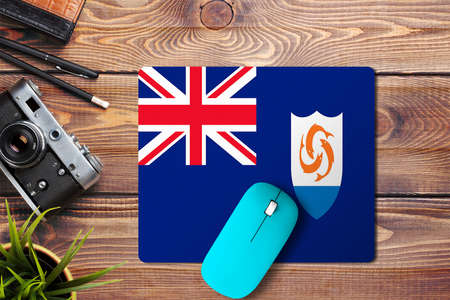 Anguilla flag on wooden background with blue wireless mouse on a mouse pad, top view. Digital media concept.の写真素材
