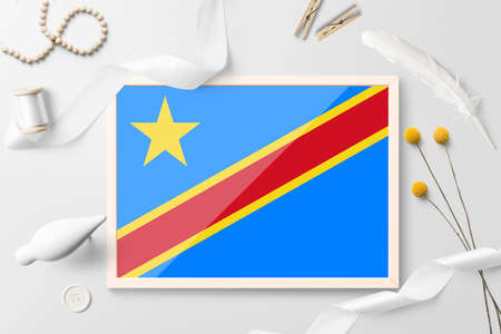 Congo flag in wooden frame on white creative background. White theme, feather, daisy, button, ribbon objects.の写真素材