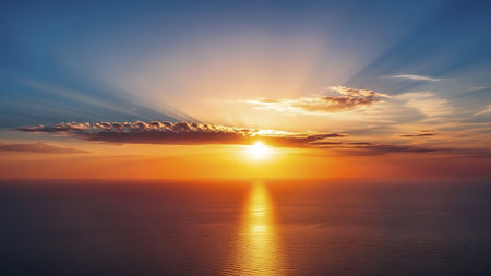 A serene image of the sun setting over a calm body of water, casting a warm glow across the sky and reflecting on the water's surface.の素材