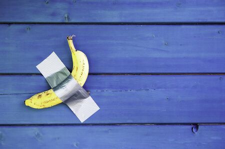 Yellow banana duct-taped to a blue wooden wall - Concept of potassium and healthy lifestyle with seasonal fruit - Vitamins and vegan lifestyle for health people - Modern art and world trade conceptの写真素材