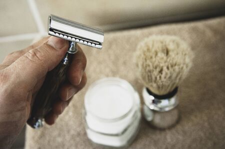 Close-up of safety razor 50s style and male cosmetic products and supplies used by men to shave. Safety razor, shaving brush and foam on beige towel background. Eco friendly tools for men shaving.の写真素材