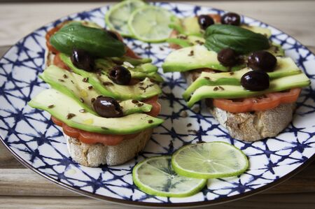 Avocado sandwich toast on ceramic vintage dish. Fresh vegetarian ingredients used on brunch meal. Bruschetta, Avocado, Tomatoes, Olives, Flaxseed, Basil, Lime. Healthy lifestyle. Raw food concept.の写真素材