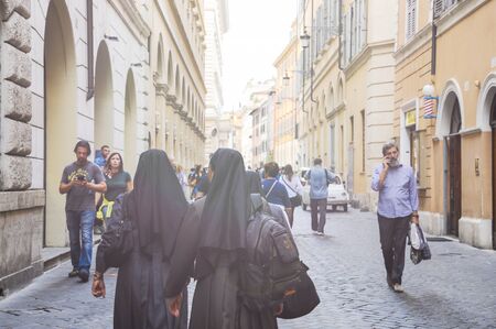 Nuns in black clothes walking down the street of Rome among tourists - Street of Rome known for the purchase of religious objects and frequented by priests, bishops and nunsの写真素材