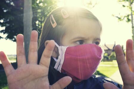 Little caucasian girl wearing medical handmade face mask protect for fine dust and as protection new coronavirus - Little girl with raised hands and big afraid eyes wearing pink face mask outdoorsの写真素材