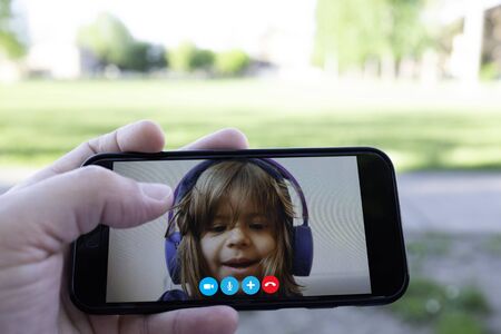 Father and daughter talking to each other through a video call on a smartphone - Hand holding a smartphone with a little girl face - Distance relationship - Childhood concept - Divorced dadの写真素材