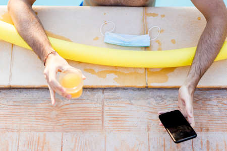 Top view of a young man having fun on poolside videocalling his friends with smartphone, drinks...