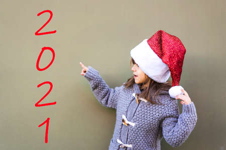 Happy cute little girl wearing santa hat pointing at copy space standing isolated on green background for 2021 new year - Happy 2021 New Year celebration concept - Finished product with textの写真素材