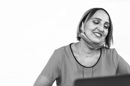 Smiling woman 40 years old wearing open protective face mask using laptop during the end of outbreak - Female entrepreneur or influencer happy for the end of pandemic - Remote work conceptの写真素材