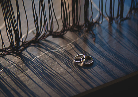 Wedding rings on a wooden board, with long shadows from tulle.の写真素材