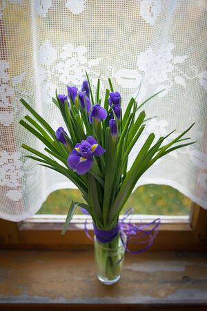 Purple iris flowers in vase, on wooden table near the windowの写真素材