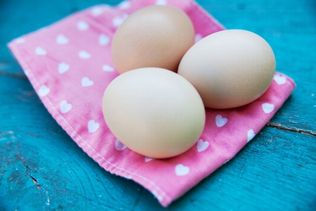 Eggs on pink tablecloth over old blue wooden background.の写真素材
