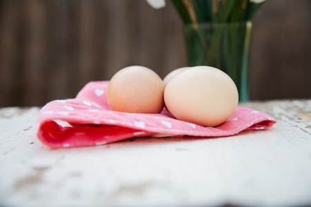 Eggs on pink tablecloth over white wooden background and vaseの写真素材