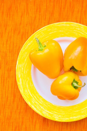 Three bright yellow peppers on a plate close upの写真素材