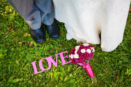Pink sign of love and bridal bouquet on the grass as well as the bride and groom feetの写真素材