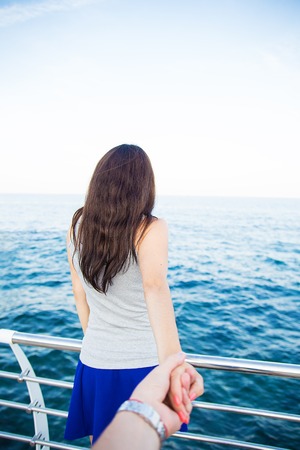 Woman sitting at the harbour on the quay with her back to the camera looking out at the moored boats, shallow dofの写真素材