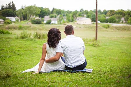 bride and groom sitting on the grass backの写真素材