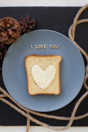 sandwich for breakfast in the form of heart with cheese on a blue plate and black background with cones inscription I love youの写真素材