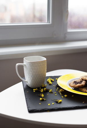 Oatmeal cookies with chocolate on bright yellow plate and cup of coffeeの写真素材