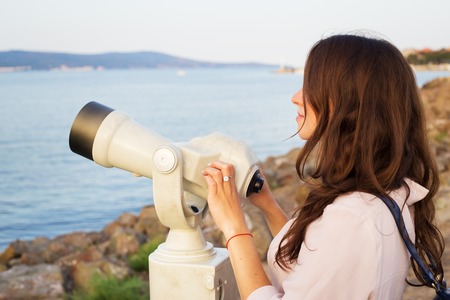The girl looks through the telescope at the seaの写真素材