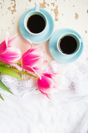 two cups of coffee and pink tulips on an old table.の写真素材
