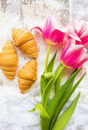 Three croissants and bright pink tulips on lace tablecloth.の写真素材