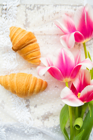 Three croissants and bright pink tulips on lace tablecloth, close-up.の写真素材