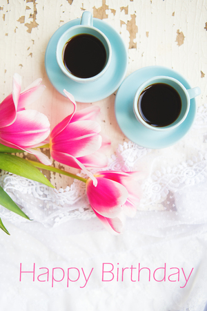 two cups of coffee and pink tulips on an old table, writing happy birthday.の写真素材