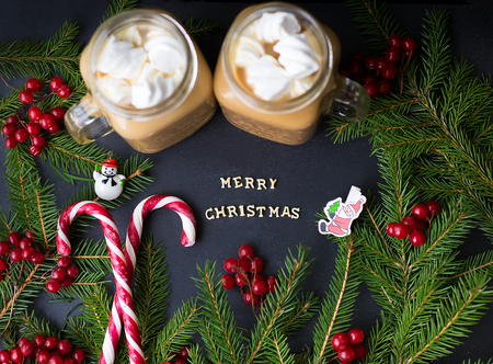 Candies and cocoa with marshmallows on a black background with the branches of trees. The inscription Merry Christmas.の写真素材