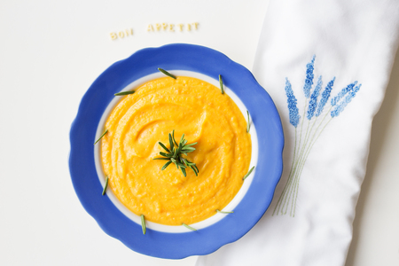 pumpkin soup in a blue plate on a napkin with flowers.の写真素材