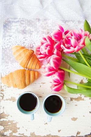 nice cup of coffee, croissants and pink tulips on old white table, close-up.の写真素材