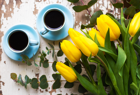 two blue cup of coffee with yellow tulips on an old tableの写真素材