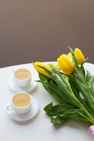 Beautiful yellow tulips on the table, two cups of tea greenの写真素材