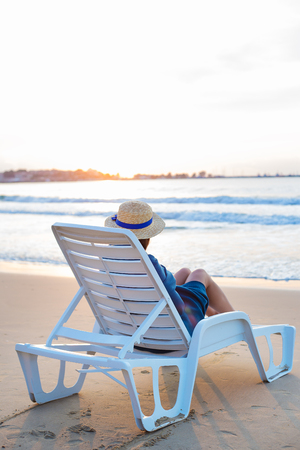 Beautiful girl in a hat sits on a deckchair meeting the dawn.の写真素材