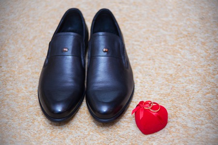 Wedding rings in a beautiful red box, and the grooms shoes.の写真素材