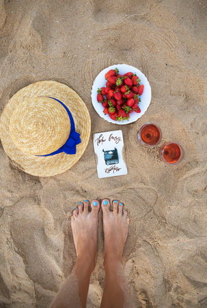 picnic on the beach - straw hat, wine and a plate of strawberries on a sandy beach.の写真素材
