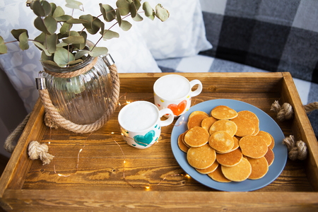 Tasty punkakes and two cups of coffee stand on a wooden tray.の写真素材