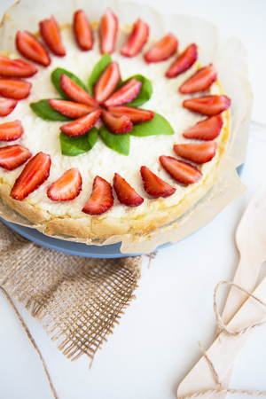 Very beautiful summer cheesecake decorated with strawberries - stands on a white wooden table.の写真素材