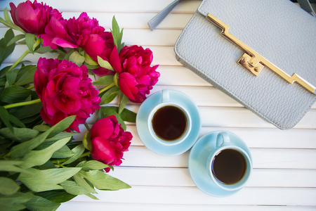 a large bouquet of beautiful peonies lies on a white table together with a blue bag and coffee.の写真素材