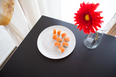 Sushi roll with salmon, philadelphia on a white plate. Red flower in a vaseの写真素材