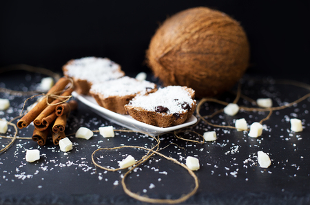 coconut muffins on a black background with cinnamon sticks and whole coconut slices and candiedの写真素材