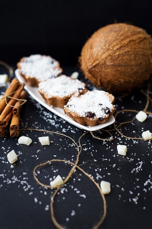 coconut muffins on a black background with cinnamon sticks and whole coconut slices and candiedの写真素材