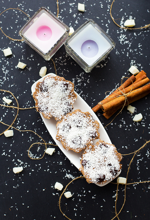 coconut cupcakes and candles on a black background with cinnamon sticks and bits of candied fruitの写真素材