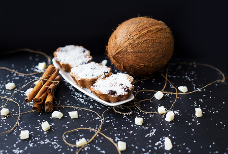 coconut muffins on a black background with cinnamon sticks and whole coconut slices and candiedの写真素材