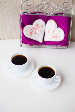 two cups of coffee and biscuits in the form of heart on a pink napkin.の写真素材