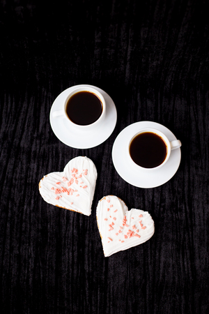 on a black background are two cups of coffee and biscuits in the form of heart.の写真素材