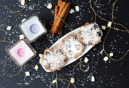 coconut cupcakes and candles on a black background with cinnamon sticks and bits of candied fruitの写真素材